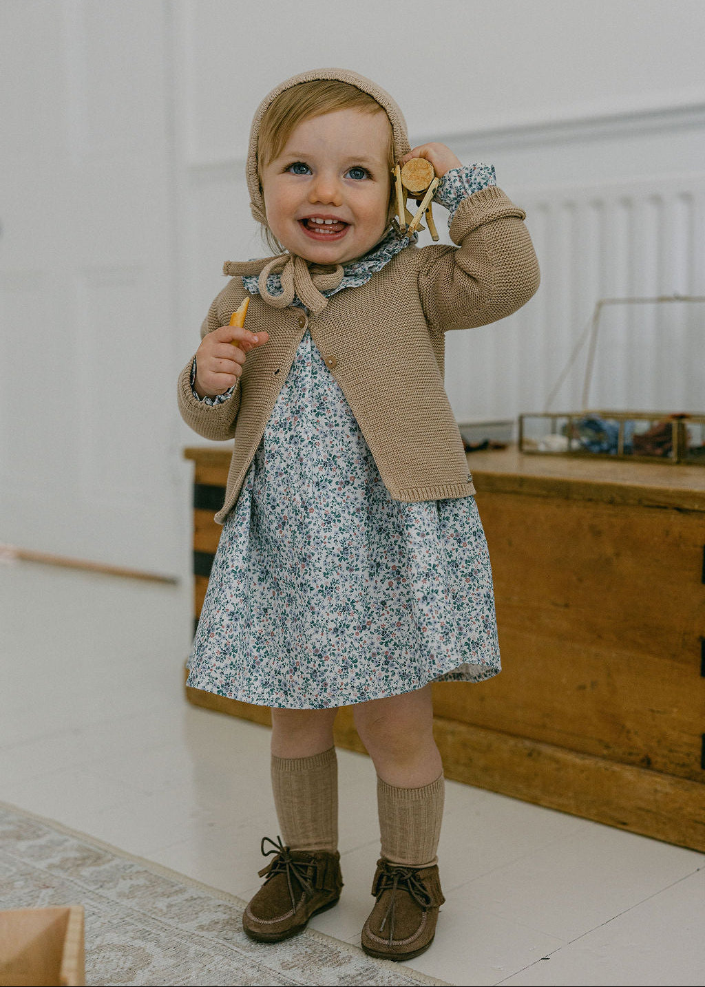 Child wearing a floral dress with a brown cardigan and boots indoors.