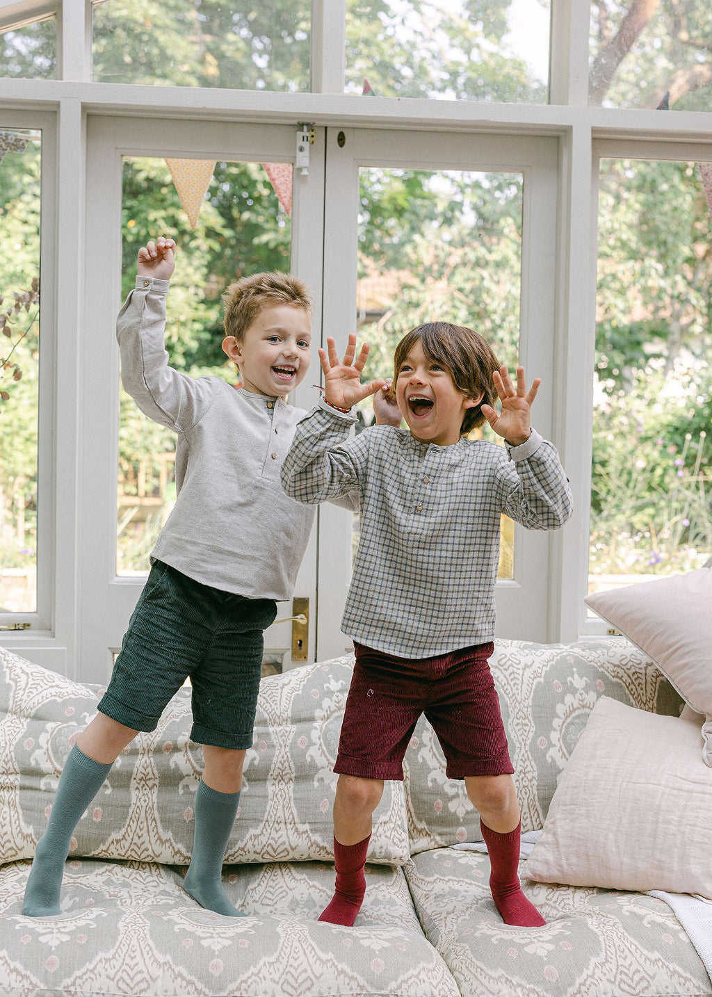 Two children playing on a couch with a large window in the background