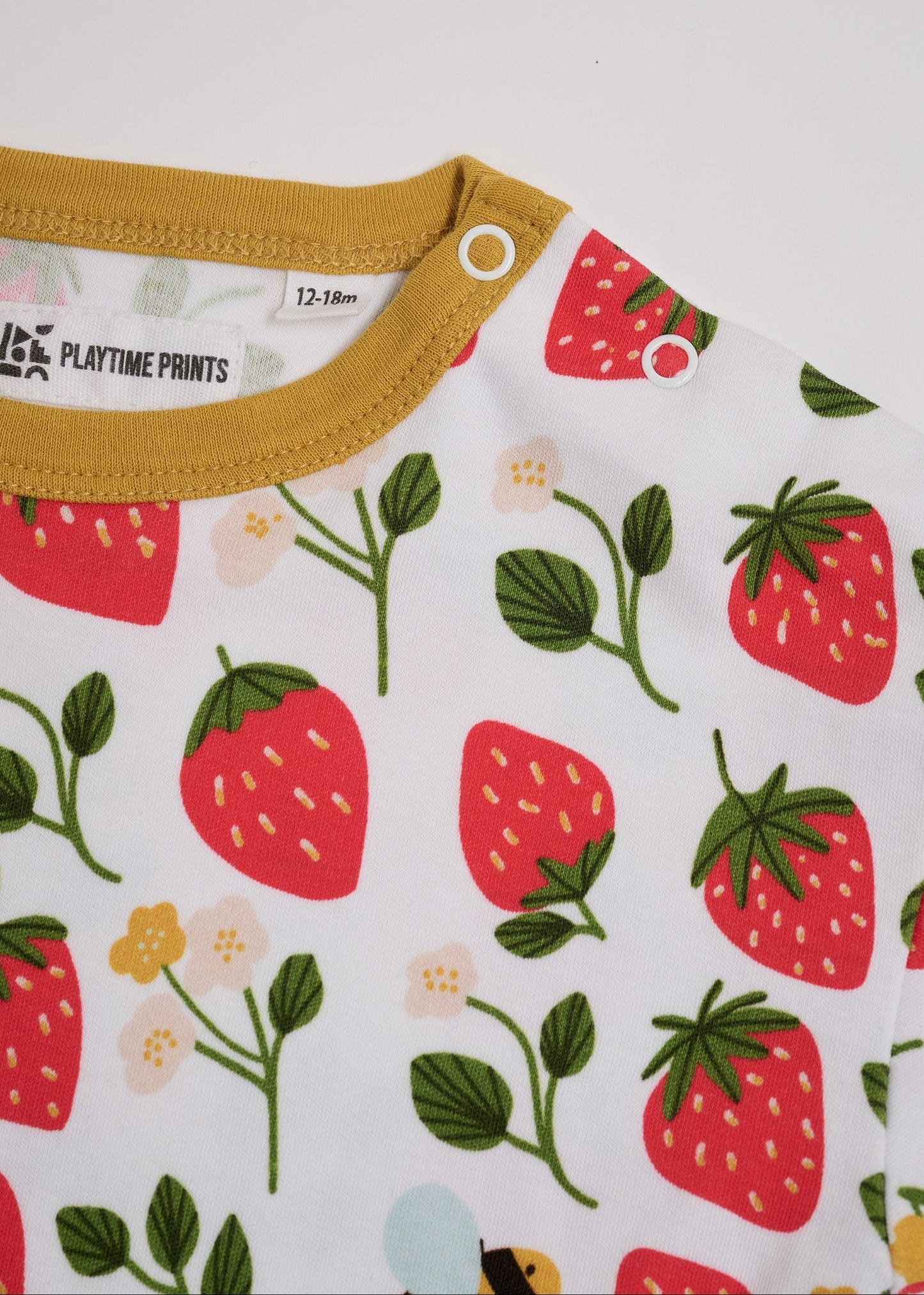 Close-up of neck poppers on a short sleeved t-shirt featuring an all over strawberry and bees print with contrast honey neck and sleeve trim.