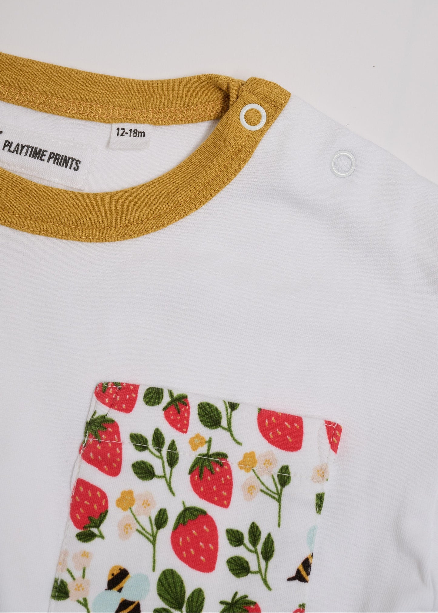 Close-up of neck poppers on white t-shirt with fun strawberry and bees square chest pocket and honey neck trim.