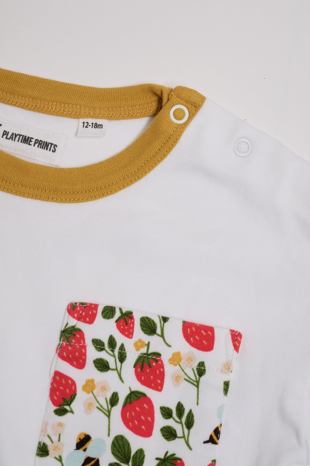 Close-up of neck poppers on white t-shirt with fun strawberry and bees square chest pocket and honey neck trim.