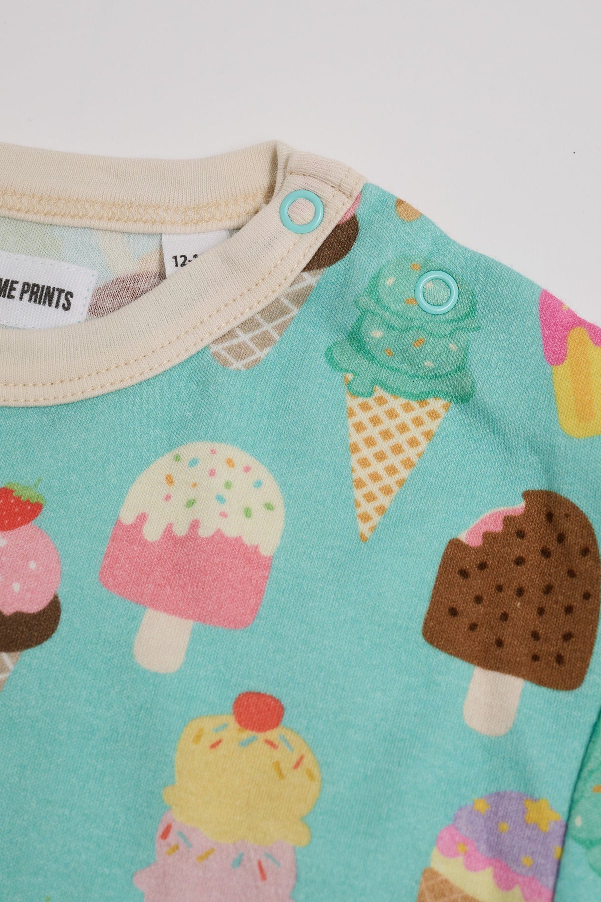 Close-up of neck poppers on a short sleeved t-shirt featuring an all over turquoise ice cream print with contrast ecru neck and sleeve trim.