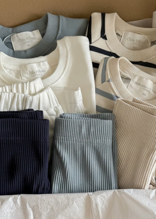 Folded clothing items including shirts and pants on a white surface.