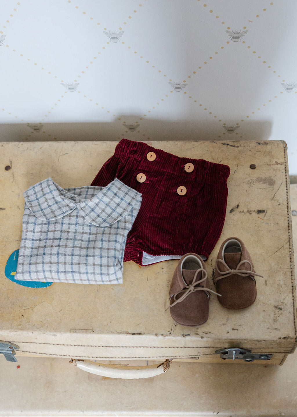 Children's clothing and shoes on an old suitcase with a patterned wall in the background