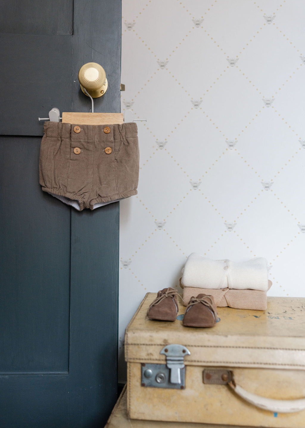 Brown shorts hanging on a door handle next to a wooden suitcase with shoes and clothes on a table.