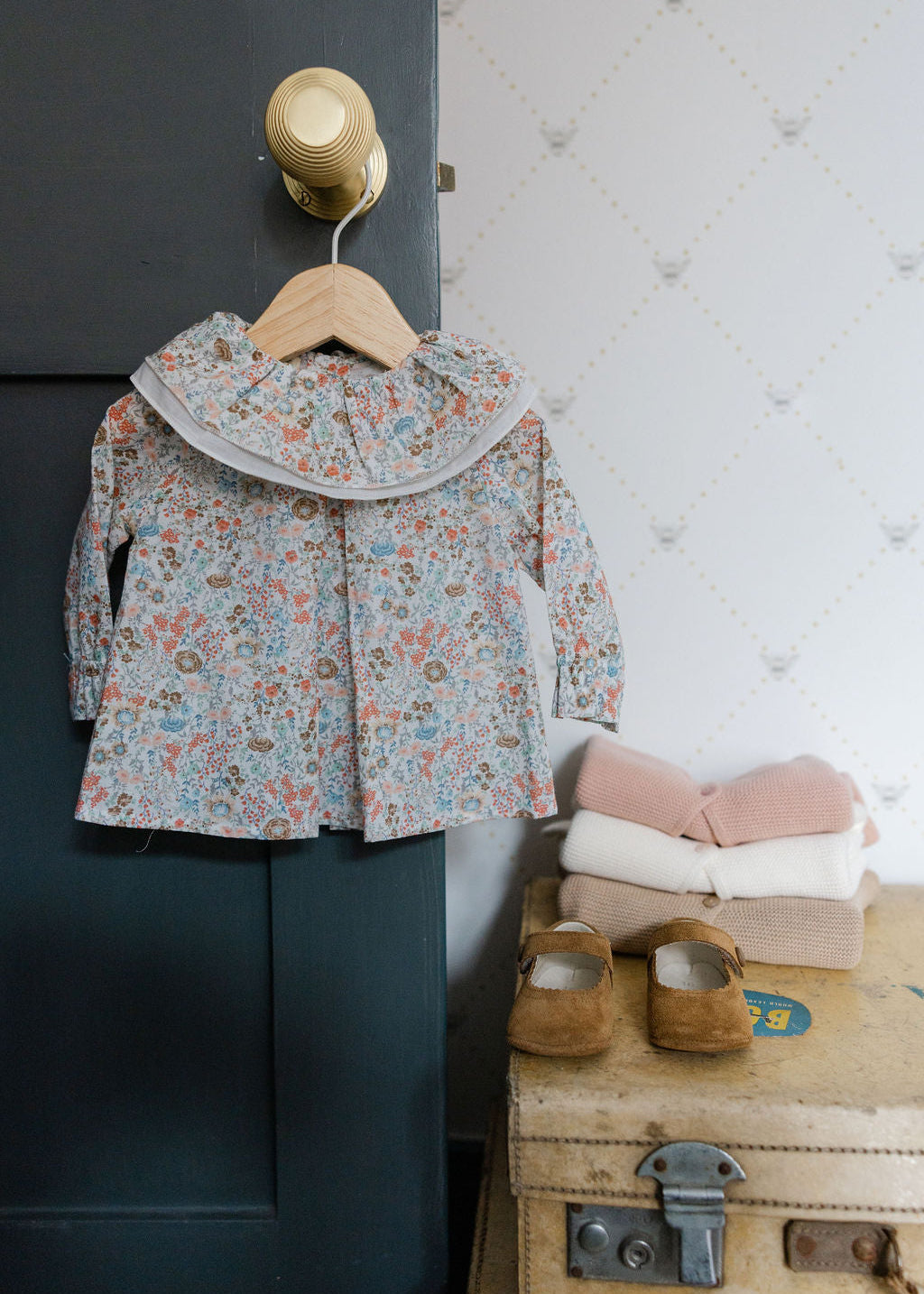 Floral jacket on a hanger next to a suitcase with shoes and blankets on a textured wall background