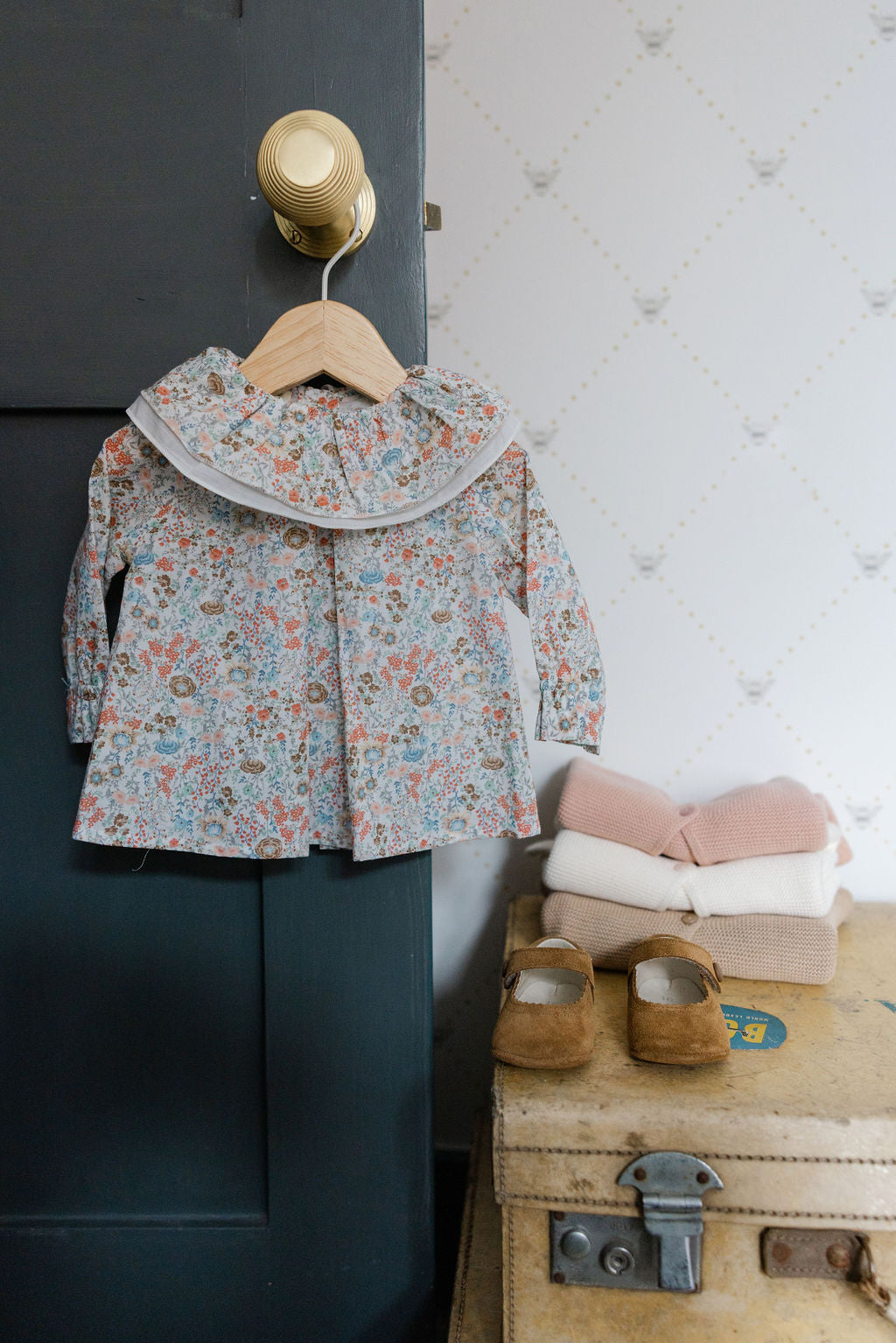 Floral jacket on a hanger next to a suitcase with shoes and blankets on a textured wall background