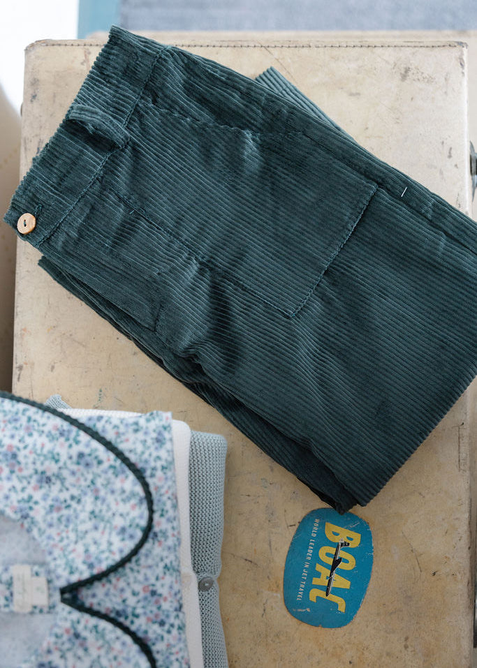 Green corduroy pants on a wooden surface with a floral-patterned garment in the background.