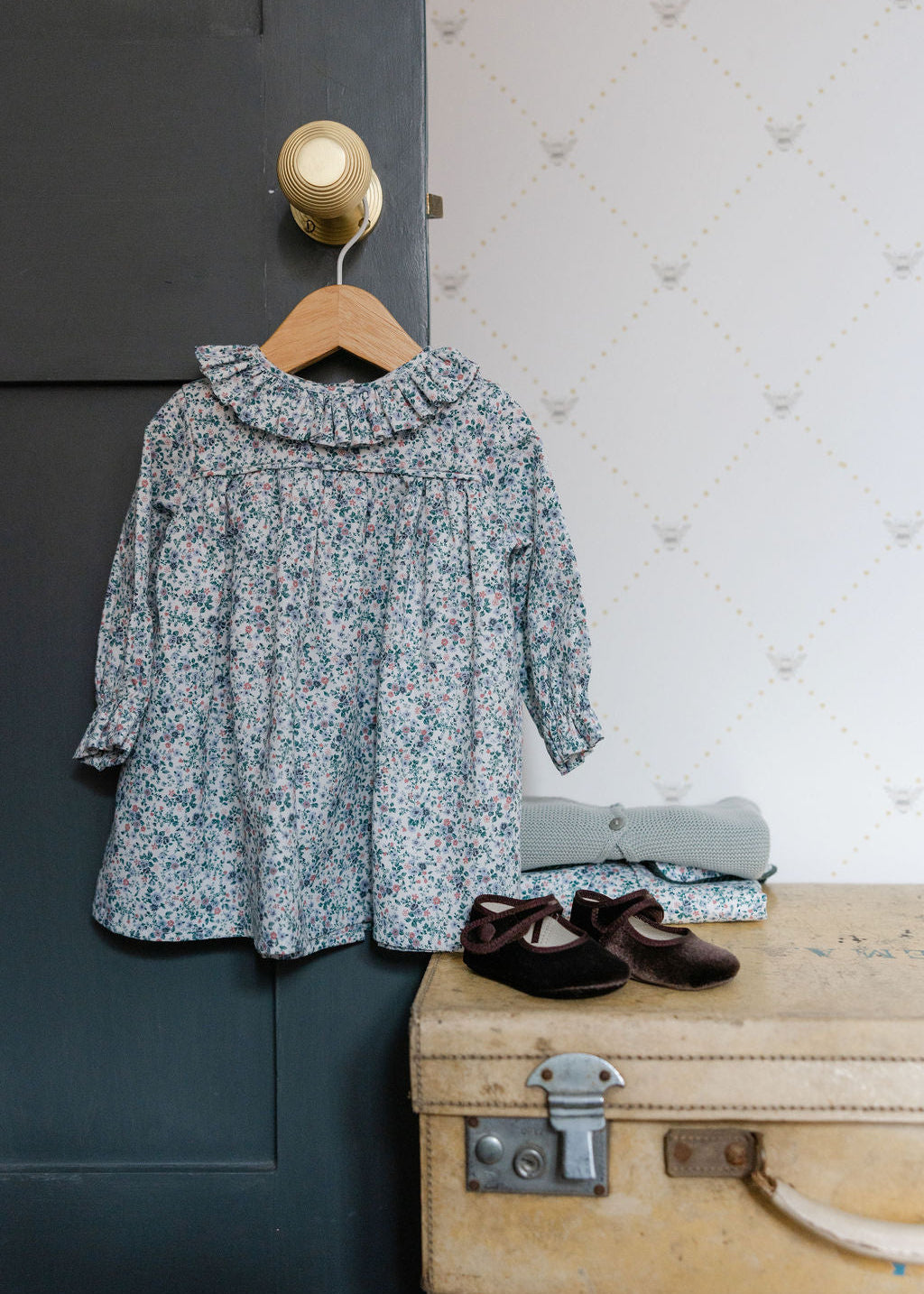 Floral dress on a hanger next to a suitcase with shoes on a textured wall background