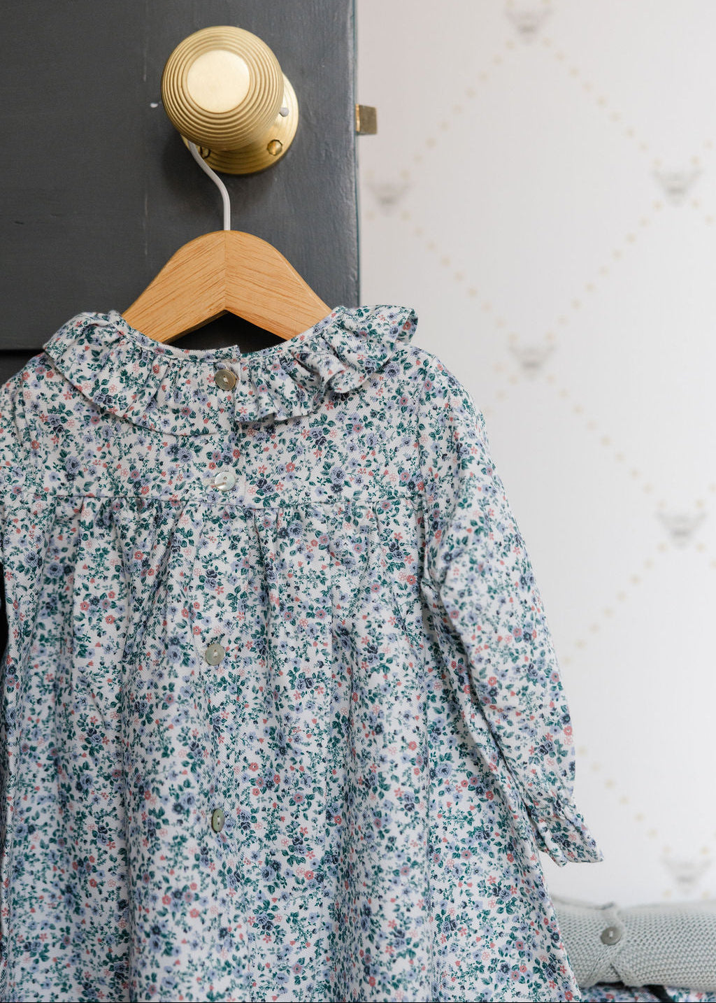 Floral dress hanging on a wooden hanger against a textured wall.