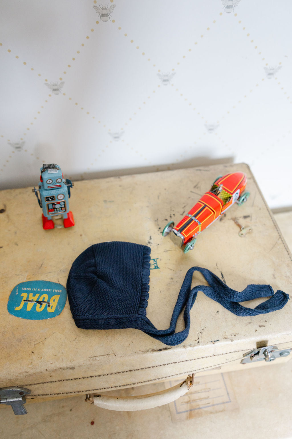 Vintage suitcase with a blue bonnet, orange toy car, and robot on a light background
