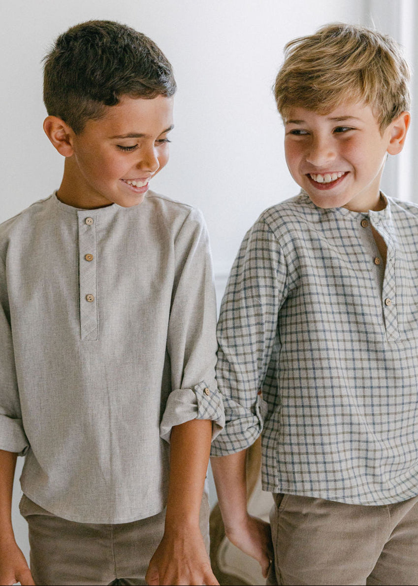 Two young boys standing side by side, smiling and wearing matching outfits.