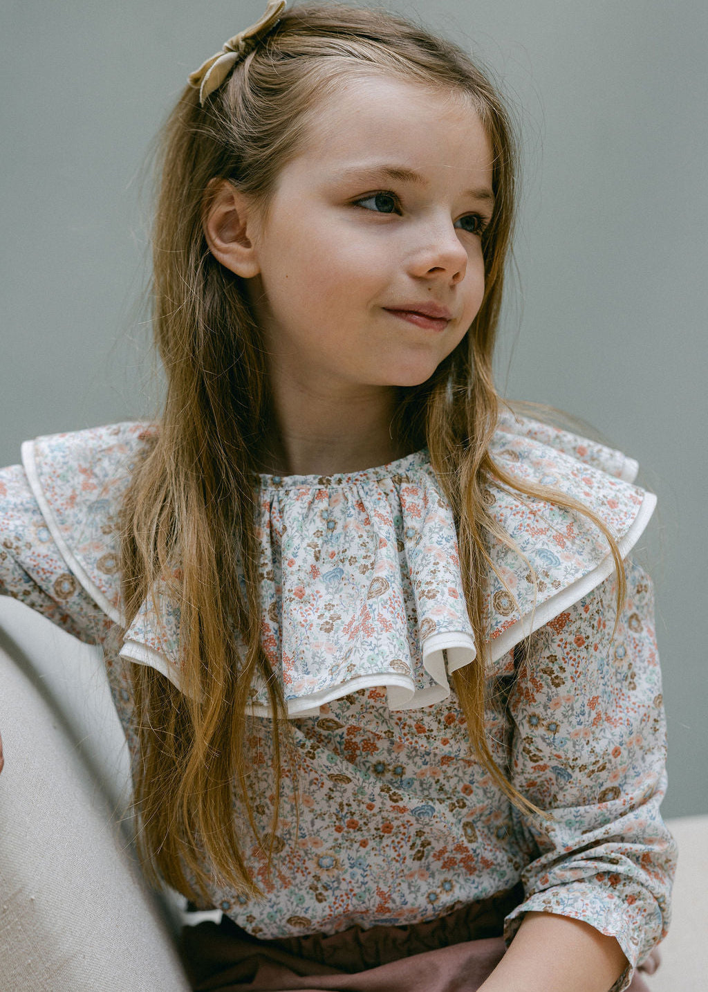 Young girl wearing a floral blouse with ruffled collar against a neutral background