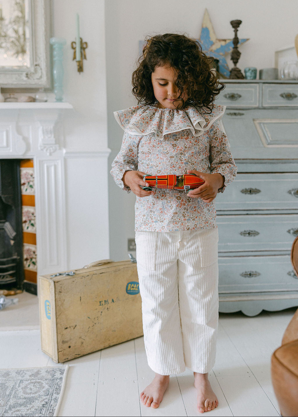 Child holding a toy in a room with a fireplace and dresser.