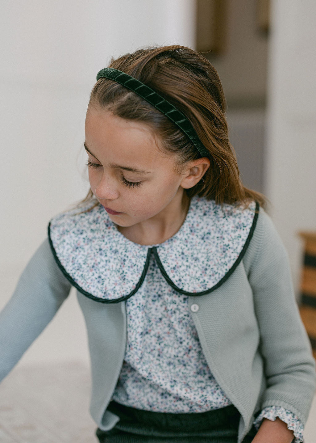 Young girl wearing a light blue cardigan with a floral collar and patterned blouse.