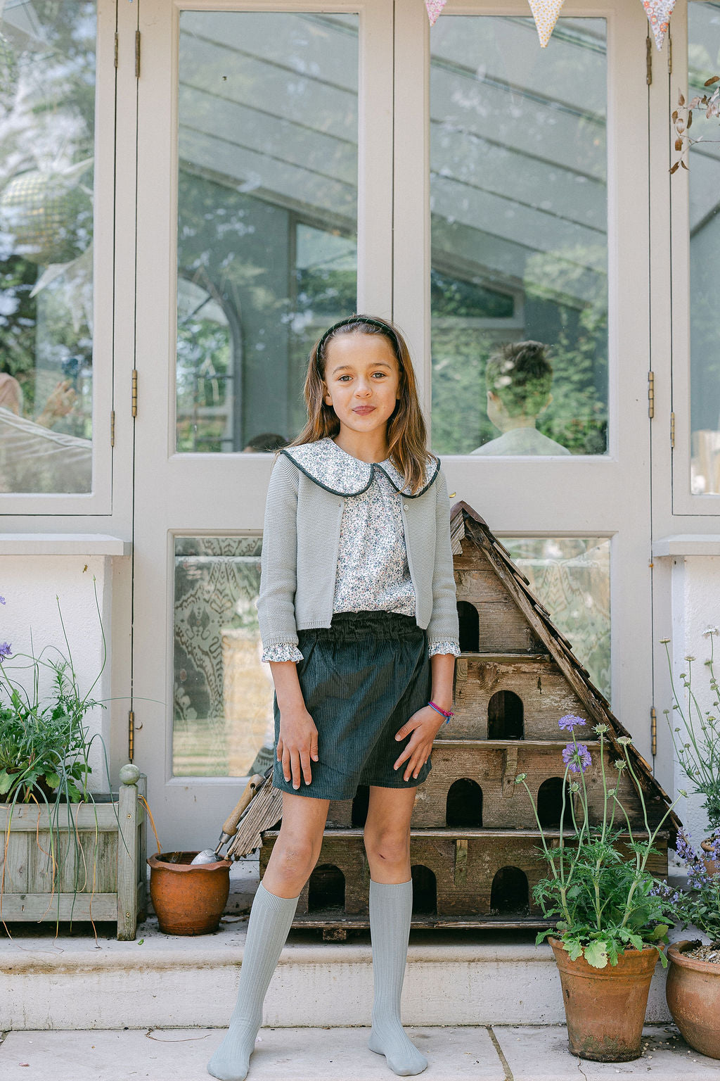 Young girl standing in a greenhouse with plants and a wooden structure in the background