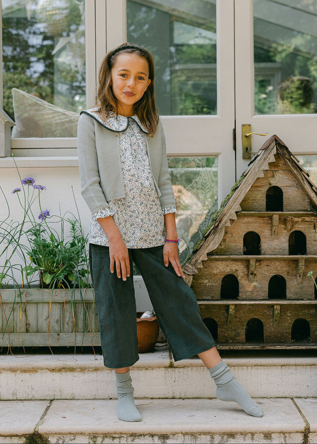 Young girl standing on steps in a garden setting with a birdhouse in the background
