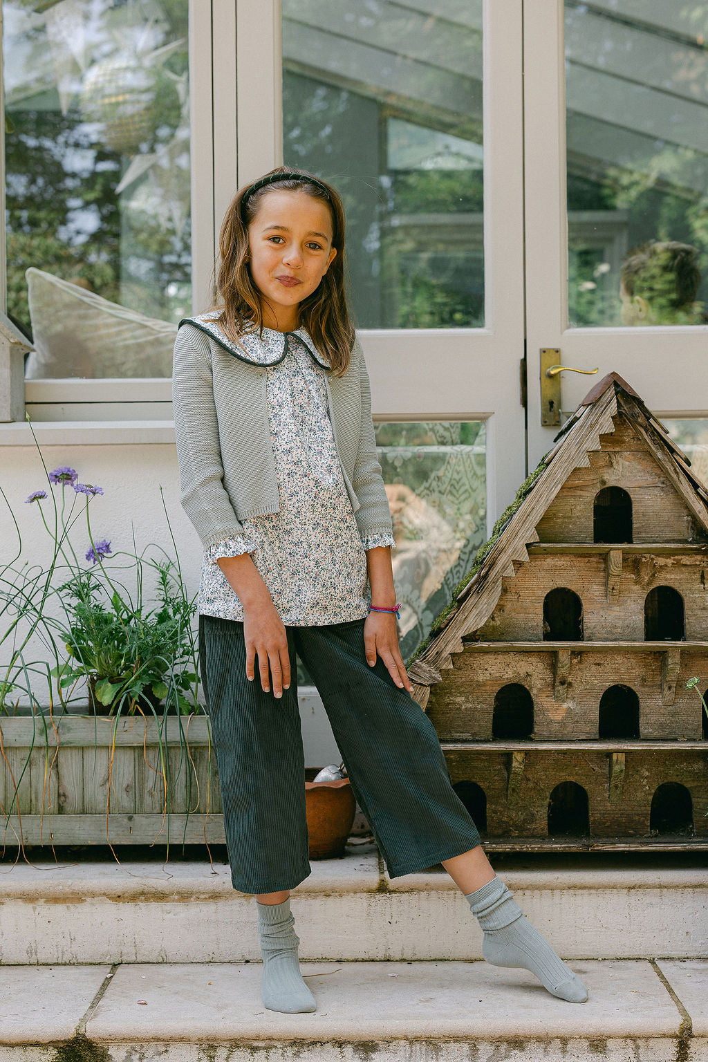 Young girl standing on steps in a garden setting with a birdhouse in the background