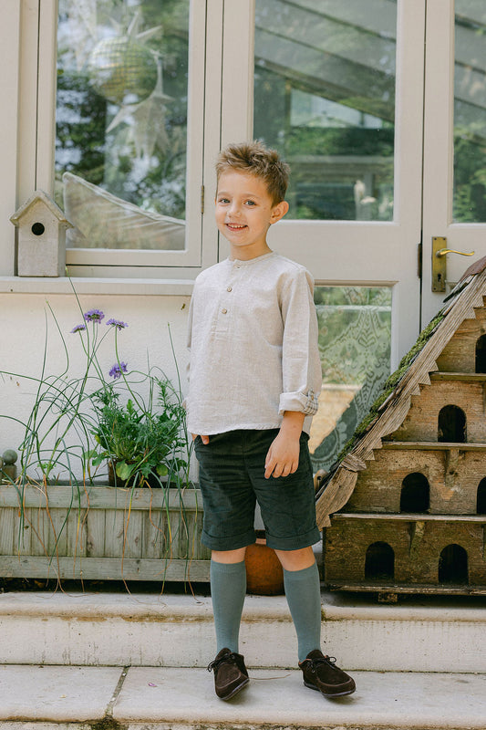 Young boy standing on a porch with a birdhouse and plants in the background