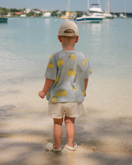 Toddler wearing a Wildgreen Lemon T-shirt from the Island Life collection. Made from 100% GOTS-certified organic cotton, this gender-neutral kids tee features a zesty lemon print, perfect for eco-conscious families who value sustainable fashion. #OrganicKidsClothing #SustainableKidswear