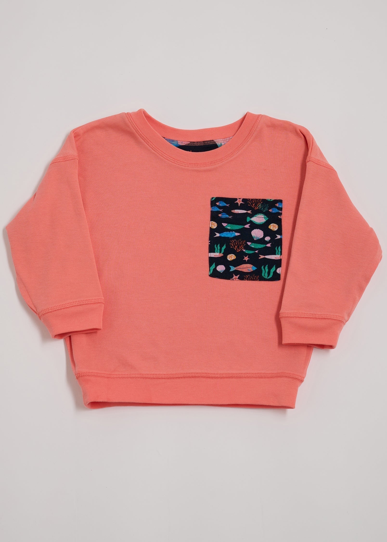 Front of coral sweatshirt with oversized vibrant navy fish print chest pocket.