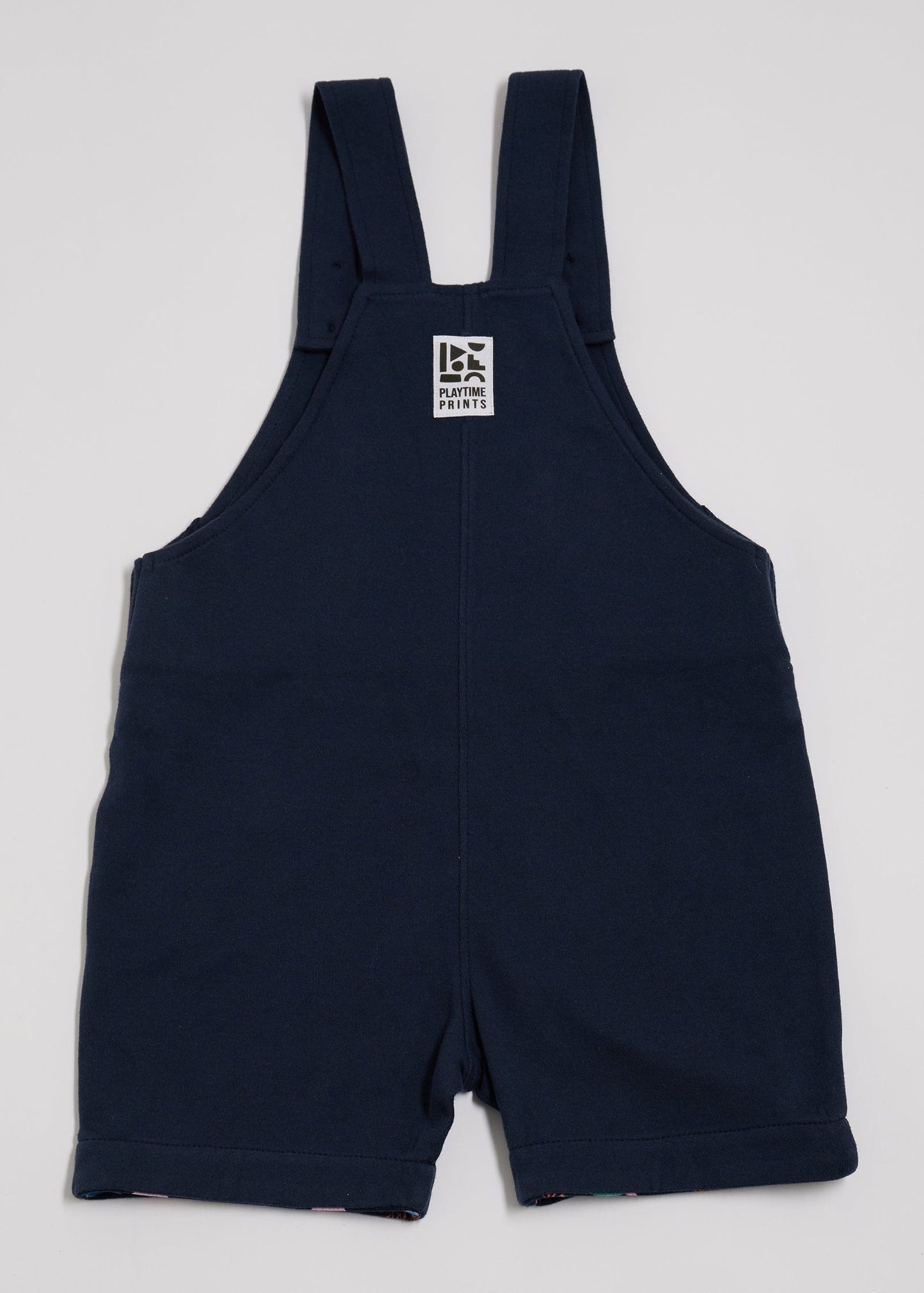 Back of navy short dungarees with Playtime Prints brand label.