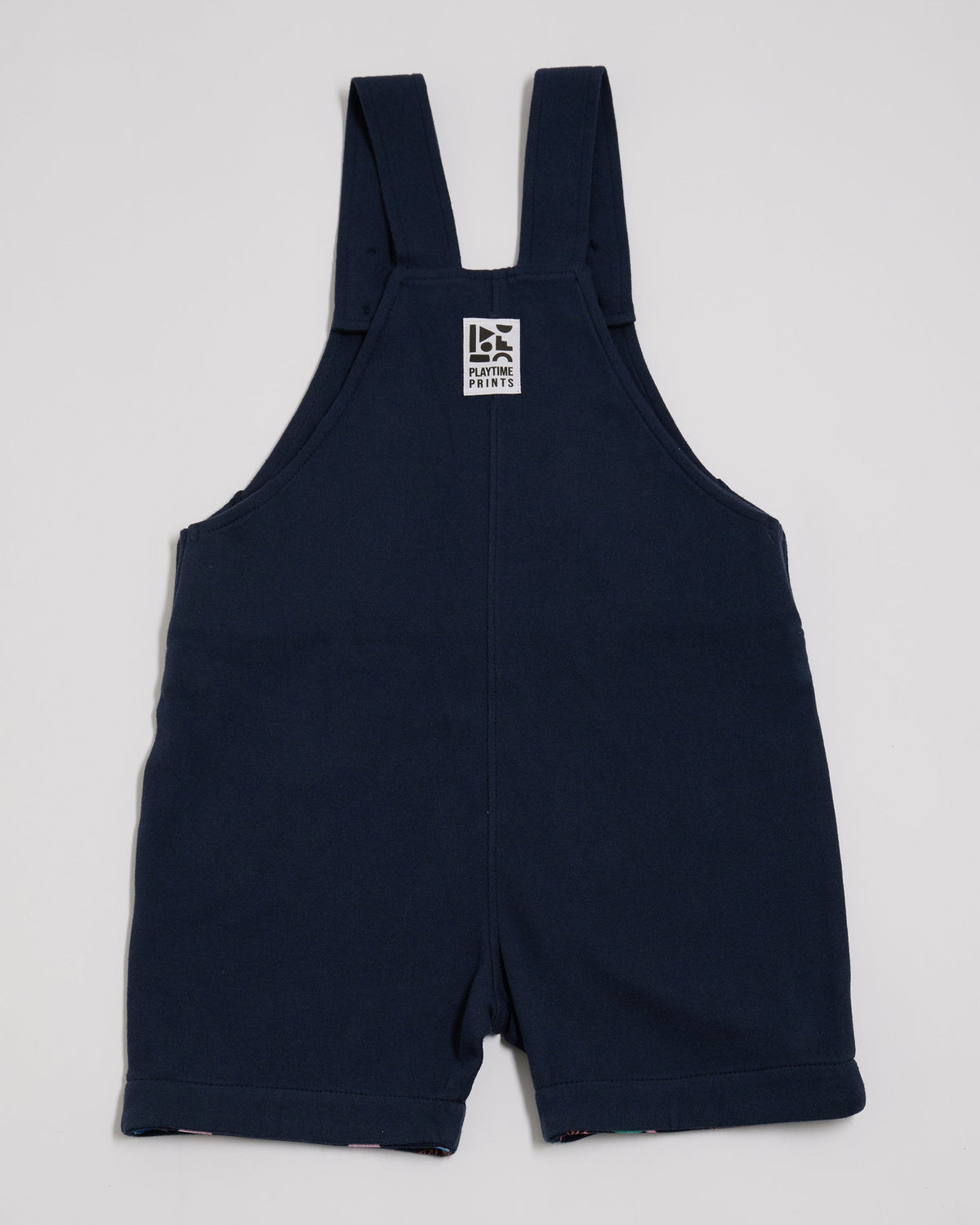 Back of navy short dungarees with Playtime Prints brand label.