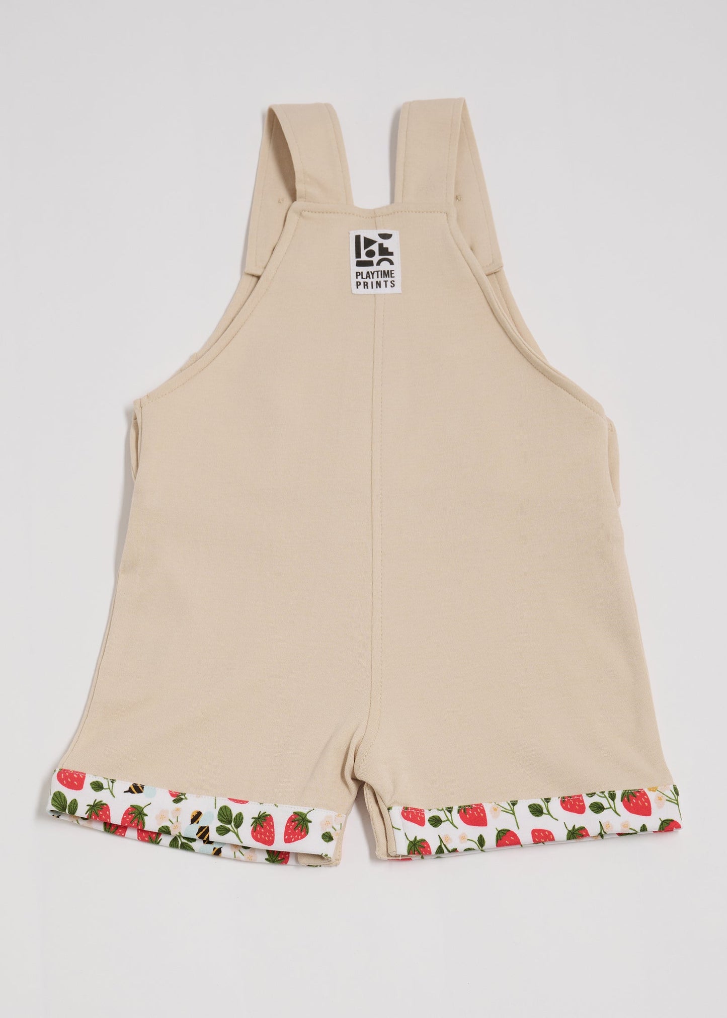 Back of beige short dungarees with fun strawberry and bee print fixed turn-ups and Playtime Prints brand label.