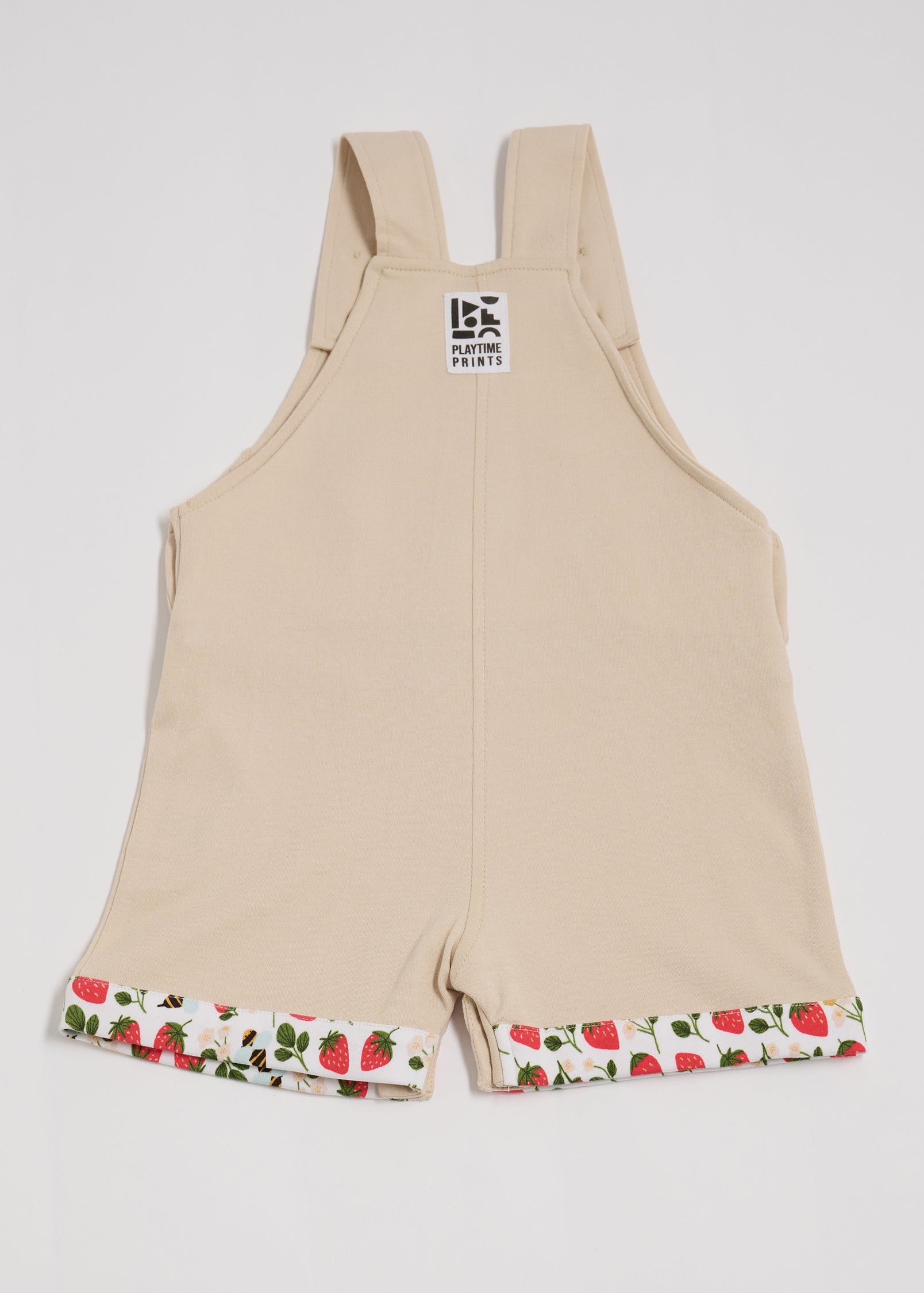Back of beige short dungarees with fun strawberry and bee print fixed turn-ups and Playtime Prints brand label.