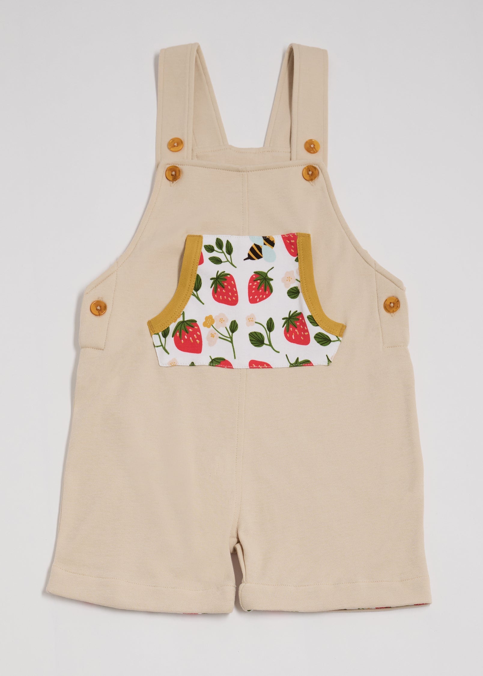 Front view of beige dungarees with fun strawberry and bees print pocket, adjustable straps, honey buttons and honey trim.