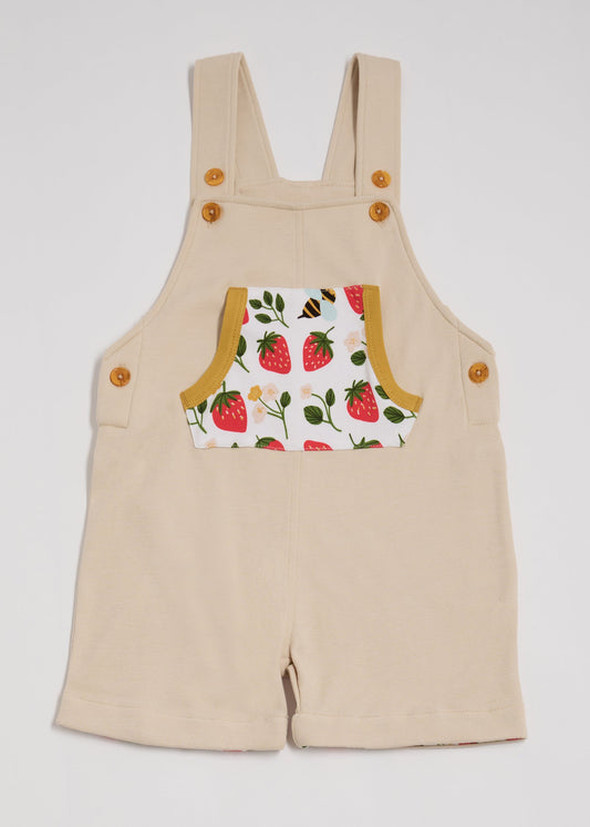 Front view of beige dungarees with fun strawberry and bees print pocket, adjustable straps, honey buttons and honey trim.
