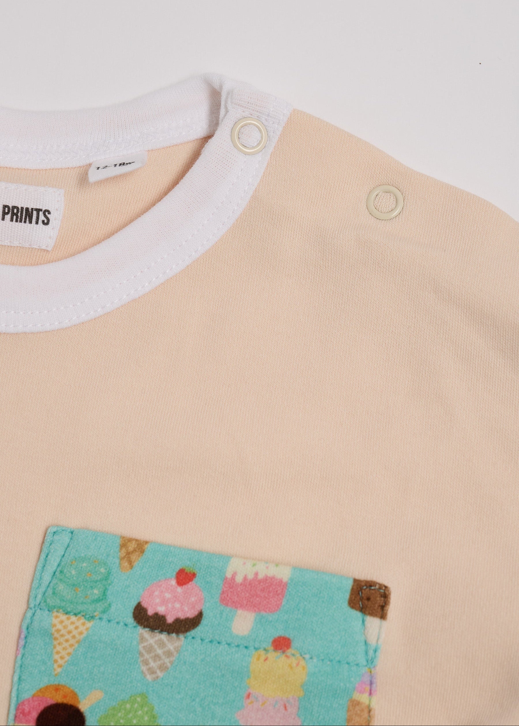 Close-up of neck poppers on vanilla coloured t-shirt with bright ice cream print square chest pocket and white neck trim.